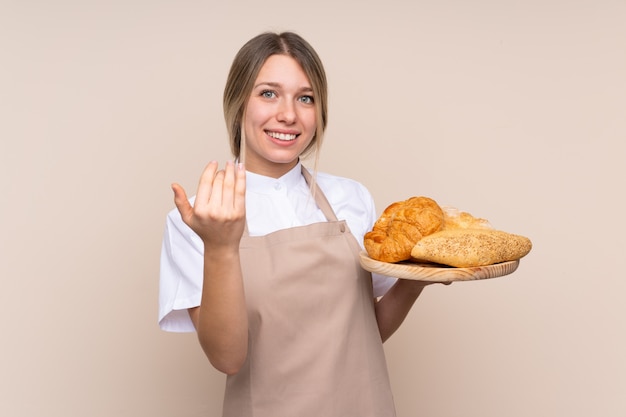 Женский пекарь держит стол с несколькими хлебами, приглашая прийти с рукой. рад, что ты пришел