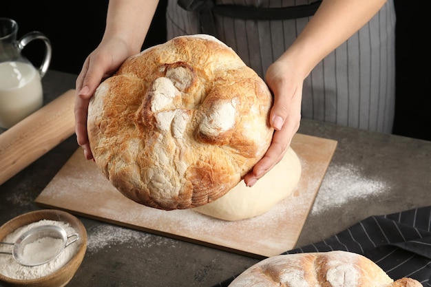 Photo female baker holding loaf of bread over kitchen table closeup