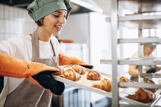 Female baker at the kitchen holding freshly baked\
croiisants