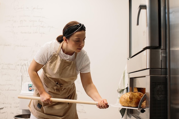 Panettiere femminile che utilizza una buccia per estrarre una pagnotta dal forno in una panetteria