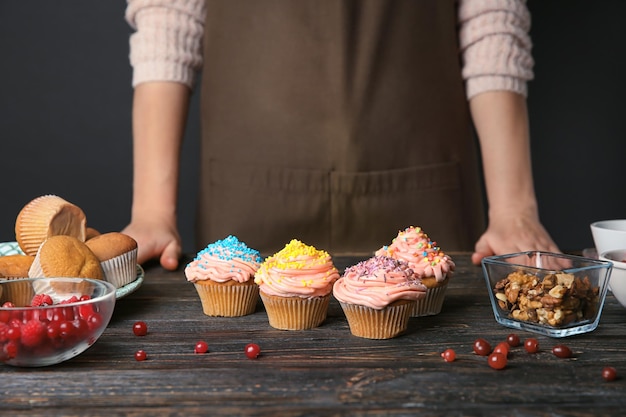 Photo female baker with decorated tasty cupcakes at table