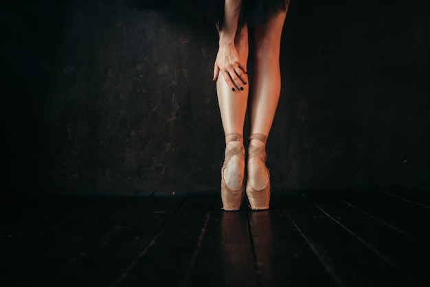 Piedini femminili del ballerino di balletto in punta, pavimento di legno nero. ballerina in abito rosso e pratica nera ballando sul palco del teatro