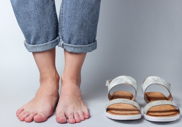 Female bare feet in jeans and sandals on white..