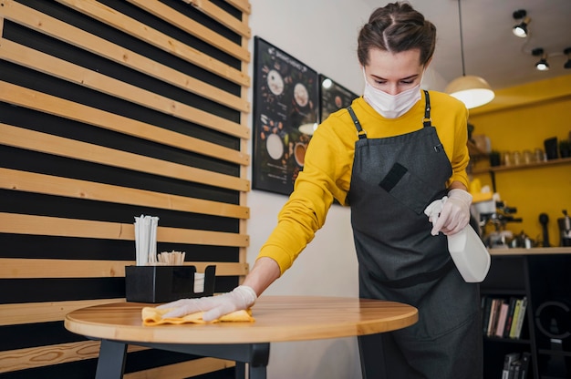 Female barista cleaning table while wearing medical mask