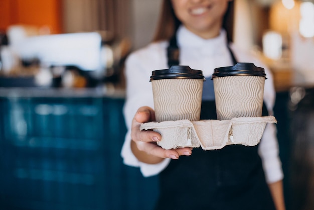 段ボールのカップで準備されたコーヒーを保持している女性のバリスタ