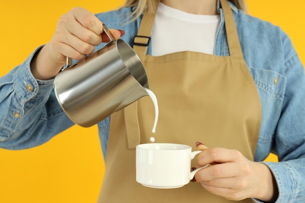 Female barista pour milk on yellow background