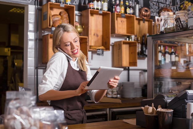 Photo female barista talking on the phone and using tablet while standing behind the counter