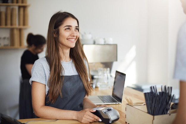 Foto barista femminile che utilizza un terminale di pagamento che parla con un cliente che riceve un ordine concetto di piccola impresa