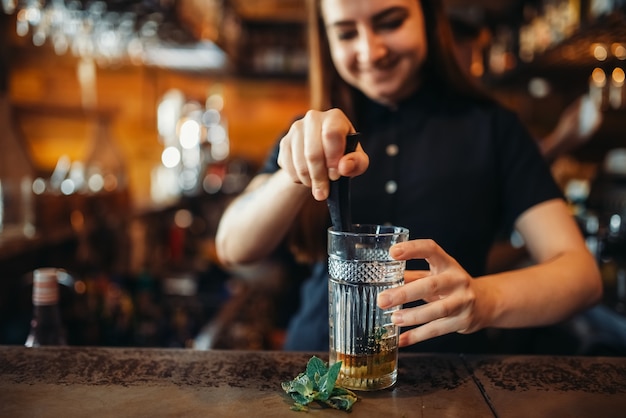 Female barman mixing at the bar counter in pub