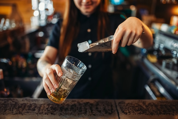 Female barman mixing at the bar counter in pub