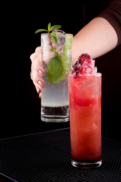 Female bartender putting mojito cocktail in rubber holder with another mixology drink facing