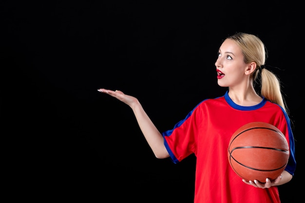 黒の背景のゲームアスリートにボールとスポーツ服を着た女性のバスケットボール選手