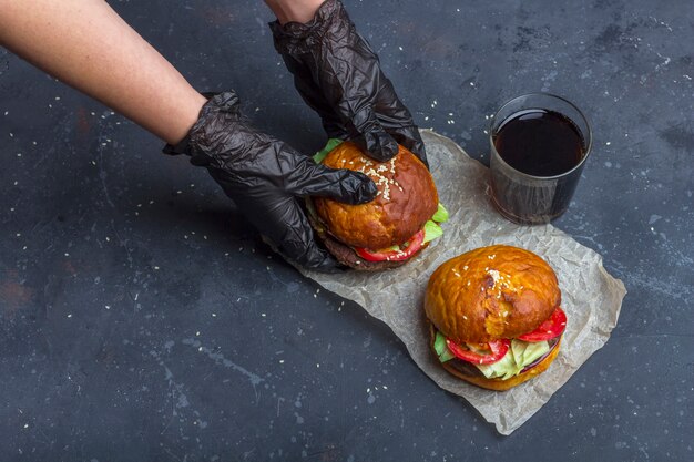 Female in black gloves holding freshly prepared grilled beef burger. American snack