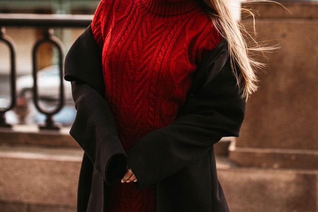 Female body in the red warm knitted sweater and black long coat Outdoor portrait in daylight Autumn winter street style cloth concept