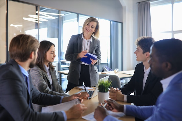 Female boss addressing meeting around boardroom table.