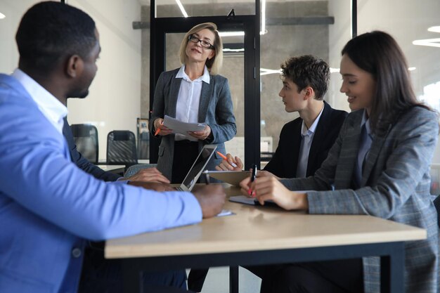 Photo female boss addressing meeting around boardroom table.