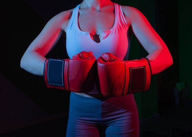 Boxer femmina con guantoni da boxe sulle sue mani in luce rossa blu al neon su una parete scura