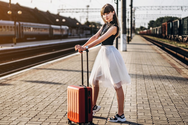 Female brunette traveler with red suitcase walking on raiway station