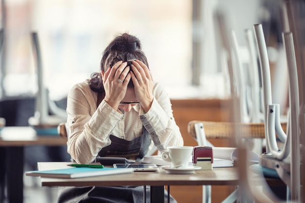 Photo female busines owner holds her head in hands in desperation over paperwork and tax declaration in a closed pub