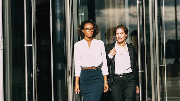 Photo female business coworkers walking out of glass door of building