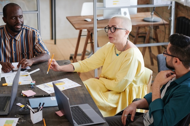 Female business leader in elegant dress talking to her employees and giving them instruction in work during a meeting at office