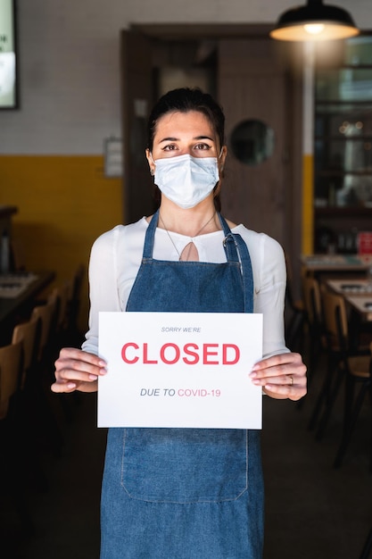 Female business owner with face mask and apron holding a sign with