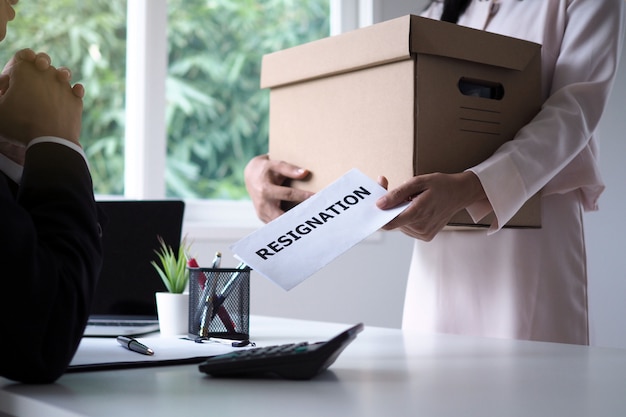 Женщина-бизнесмен держит коричневую картонную коробку и отправляет заявление об отставке руководству. Перемещение рабочих мест и вакансий