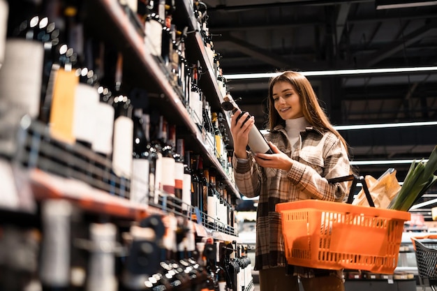 Female buyer with a basket of groceries chooses wine