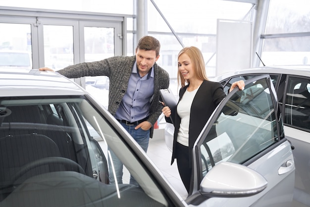 Photo female car dealer showing automobile to potential buyer.