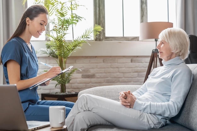 Female caregiver writing on tablet information about senior woman indoors