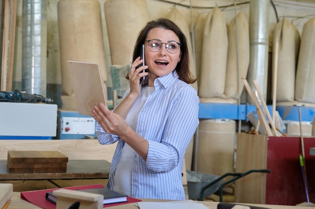 Плотник-дизайнер женского пола работает в столярной мастерской, выбирает материалы, разговаривает по телефону. Промышленный бизнес, деревообработка