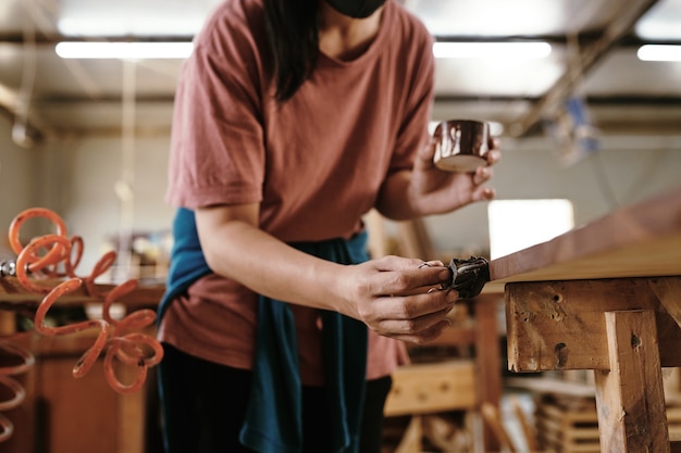 Female carpenter varnishing wood board when working on furniture item for customer