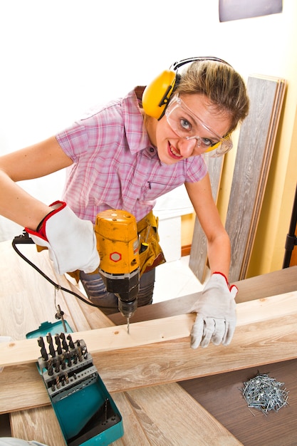 Carpentiere femminile sul lavoro facendo uso della perforatrice della mano