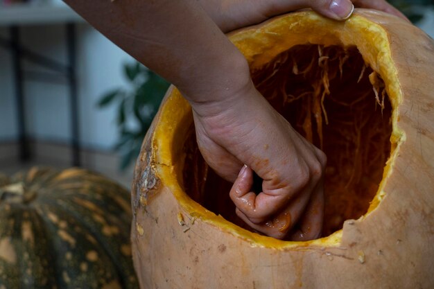 Female carving large orange pumpkin for halloween while sitting at wooden table at home