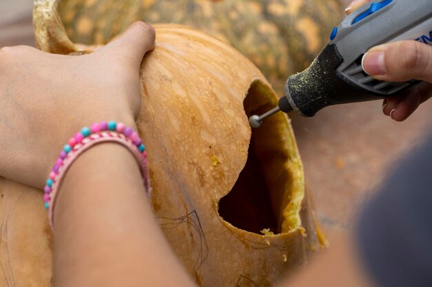 Female carving large orange pumpkin for halloween while sitting at wooden table at home