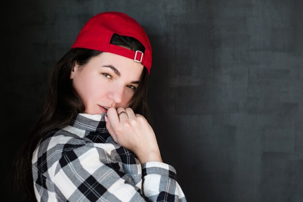  female in casual clothes red cap on head looking intently at camera. 