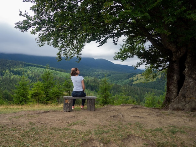 Female in casual clothes sits under large tree with forest background