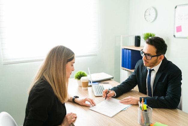 Female caucasian client and professional male lawyer checking and talking about signing a contract. Hispanic boss speaking of a business deal with his female colleague