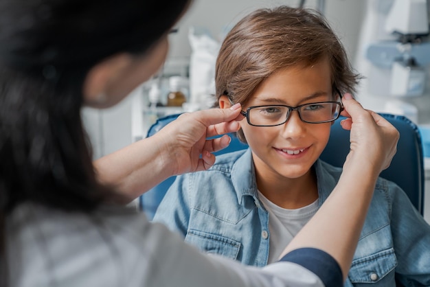 Photo female caucasian doctor putting glasses on little boy in clinic