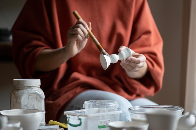 Female ceramicist or potter holding paintbrush applying glaze on ceramic pieces