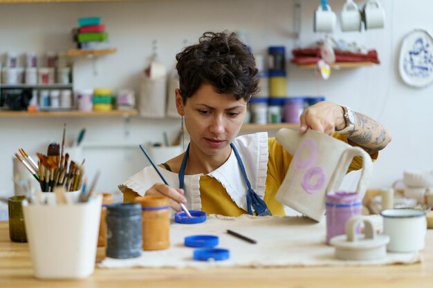 Female ceramist drawing ornament on clay teapot woman potter master painting pottery in studio