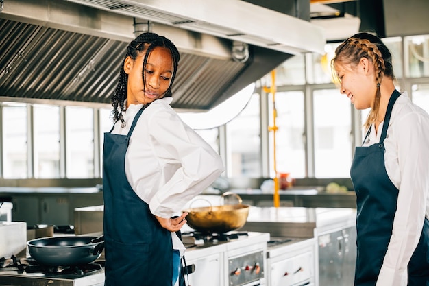 Female chef aids friend tie apron in a restaurant kitchen Two adults in uniform prepare for food education and service in a professional setup