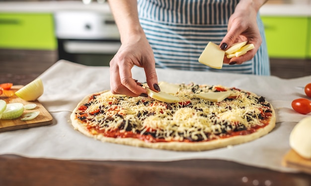 A female chef in an apron is putting mozzarella cheese on a raw pizza