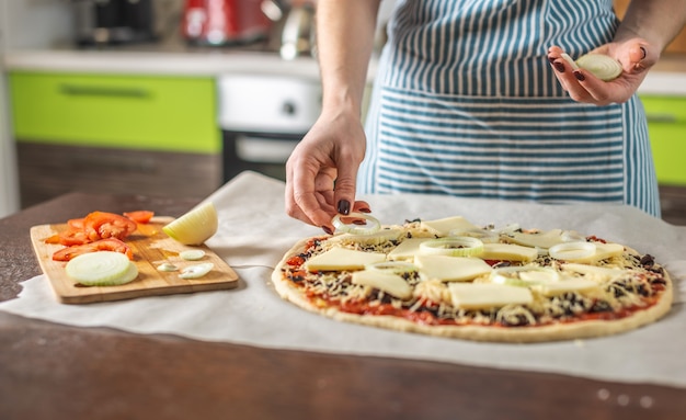Una chef donna con un grembiule sta mettendo anelli di cipolla su una pizza cruda