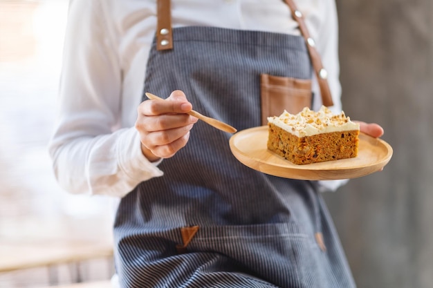 A female chef baking and eating a piece of homemade carrot cake in wooden tray