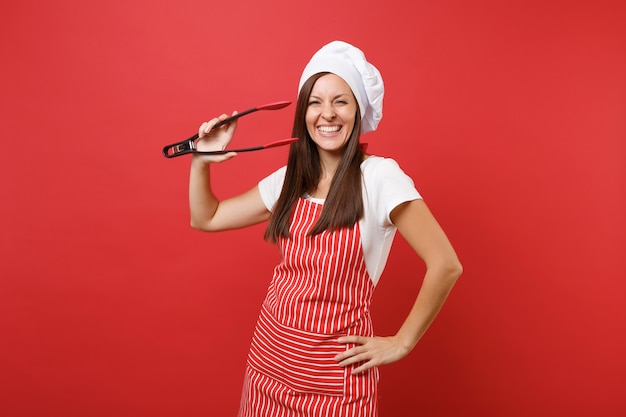 Cuoco o panettiere femminile in grembiule a strisce, cappello da chef toque t-shirt bianco isolato su priorità bassa rossa della parete. donna tenere insalata di cucina che serve plastica paio di pinze per grill. deridere il concetto dello spazio della copia.