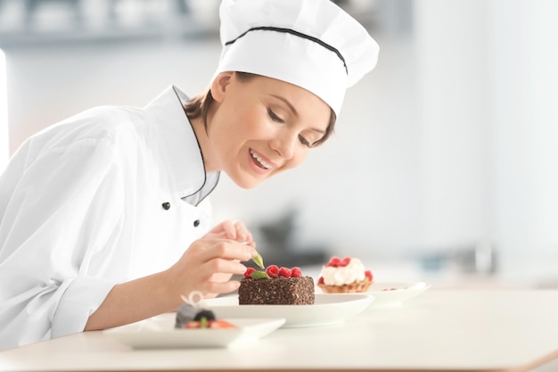 Female chef decorating tasty desserts in kitchen