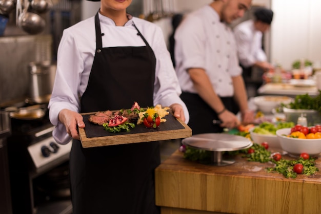 female Chef  in hotel or restaurant kitchen holding grilled beef steak plate with vegetable decoration