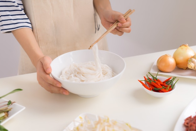 Female chef prepare traditional Vietnamese soup Pho bo with herbs, meat, rice noodles