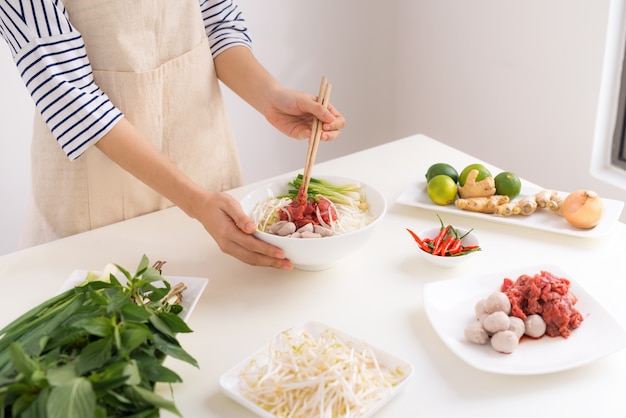 Female chef prepare traditional Vietnamese soup Pho bo with herbs, meat, rice noodles